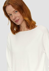 Witte blouse met lange mouwen, voorzien van een ruime halslijn en een zachte textuur. Het ontwerp heeft een subtiele naad aan de voorkant en een relaxte pasvorm.