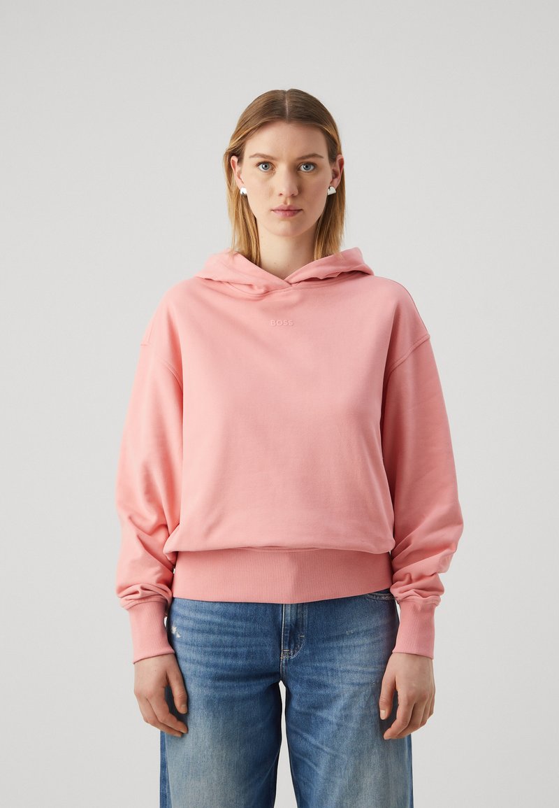 Sweat à capuche rose avec une coupe décontractée, des poignets et un ourlet côtelés. Présente un petit logo sur la poitrine, associé à un jean clair.