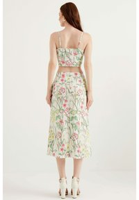 Blommig crop top och kjolset, med en vit bakgrund och rosa samt gula blommor, spaghetti-straps och en figurnära silhuett.