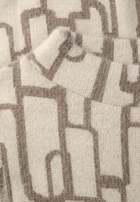 Beige stickat textil med ett geometriskt mönster i ljusbrunt, med en mjuk textur och synliga sömnadsdetaljer.