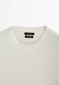 Sweater tricoté beige clair avec une texture en nid d'abeille, col rond et bords côtelés. L'étiquette affiche le nom de la marque et les instructions d'entretien.