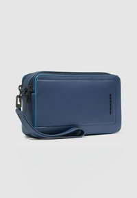 Portafoglio in pelle blu con superficie testurizzata, chiusura con zip e cinturino da polso. Presenta bordi cuciti a contrasto e dettaglio con logo.