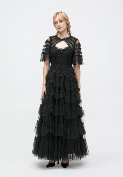 Czarna sukienka wykonana z warstwowego tiulu z falbaniastymi akcentami, krótkimi pufowymi rękawami i dekoltem w kształcie łezki. Posiada dopasowaną górę i rozkloszowany dół.