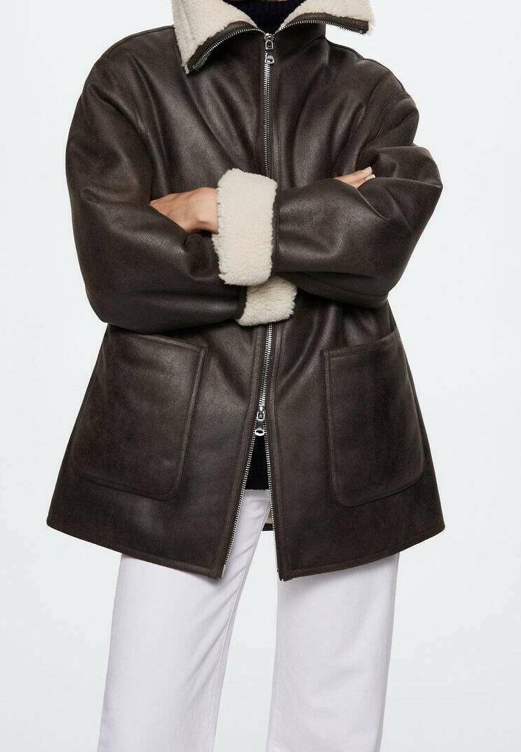 Giacca di pelle marrone con colletto e polsini in shearling, dotata di una cerniera frontale e due grandi tasche. Texture liscia e vestibilità comoda.
