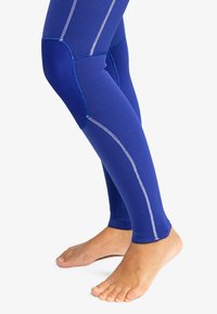 Blue athletic leggings with a textured fabric, featuring white stitching and panels at the knees, designed for flexibility and comfort.
