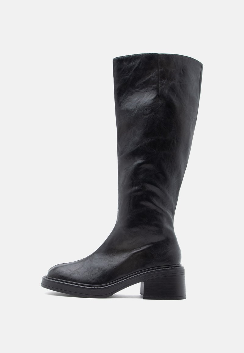 Μαύρες δερμάτινες μπότες μέχρι το γόνατο με ελαφρώς γυαλιστερό φινίρισμα, στρογγυλή μύτη και χοντρό τακούνι. Διαθέτουν ελάχιστες ραφές και λεία υφή.