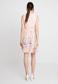 Hellrosa Blumenkleid mit tailliertem Schnitt, ausgestellt Rock und einer Mischung aus blauen und pinken Blumen; getragen mit weißen Riemchen-Absätzen.