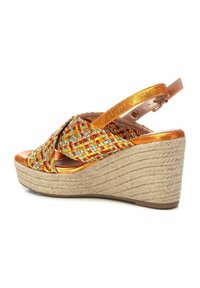 Sandalia de cuña con parte superior trenzada multicolor en rojo, amarillo y azul, con acentos metálicos y suela de cuerda natural. Correa ajustable.
