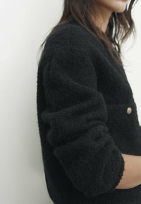 Svart stickad tröja med texturerad finish, med rund halsringning och knappdetalj, som har en lös passform och avslappnade ärmar.