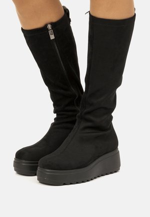 Bottes noires montantes en suède doux avec une épaisse semelle plateforme et un détail de fermeture éclair sur le côté. Texture lisse et design décontracté.