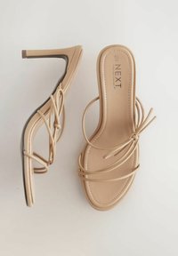 Beige High Heelsandaletten mit schlankem Riemen-Design, offenen Zehen und texturierten Sohlen. Fesselriemen verleihen dem minimalistischen Look eine besondere Note.