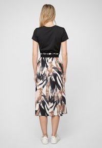 Haut noir à manches courtes associé à une jupe fluide longueur genoux avec un motif abstrait audacieux en noir, beige et blanc. Porté avec des baskets blanches.