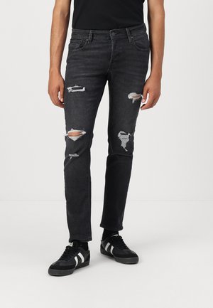 Black denim jeans with ripped details and frayed edges, slim fit, and standard five-pocket design. Paired with black sneakers.