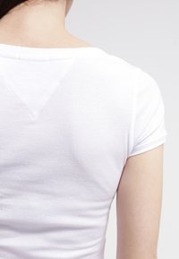 Vit kortärmad fitted t-shirt, ribbad textur, V-formad ryggslits, enkel design, klassisk stil, minimal detaljer, lättviktig tyg.