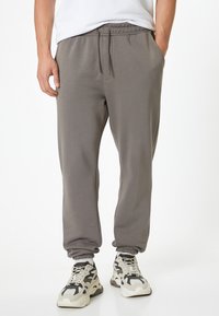 Pantalones de chándal grises con cintura elástica, bolsillos laterales y tobillos acampanados, hechos de una tela suave, combinados con zapatillas gruesas.