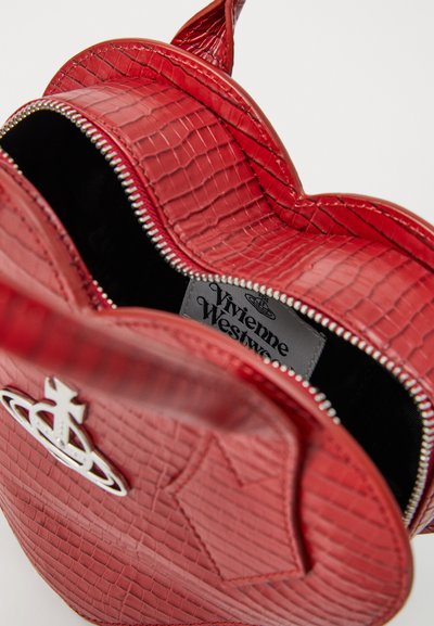 Borsa a forma di cuore rossa con texture, logo orb in argento, parzialmente zip chiusa che mostra l'interno nero e l'etichetta Vivienne Westwood all'interno.