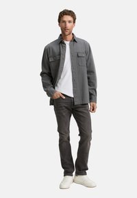 Gray shirt jacket with a button-up design, two chest pockets, worn over a white t-shirt, paired with dark jeans and white sneakers.