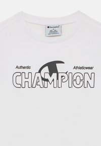 Λευκό κοντομάνικο T-shirt με στρογγυλή λαιμόκοψη, με έντονα μαύρα γράμματα που γράφουν «Authentic Athleticwear CHAMPION». Ετικέτα στο εσωτερικό.