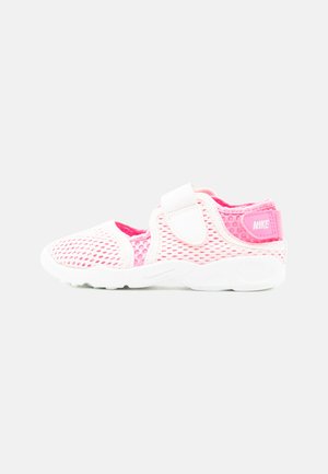 Roosa ja valge Nike laste spordijalats, mille pealmine osa on hingavast võrgumaterjalist ja millel on takjakinnitus, esitatud ühetaustalisel helehallil taustal.