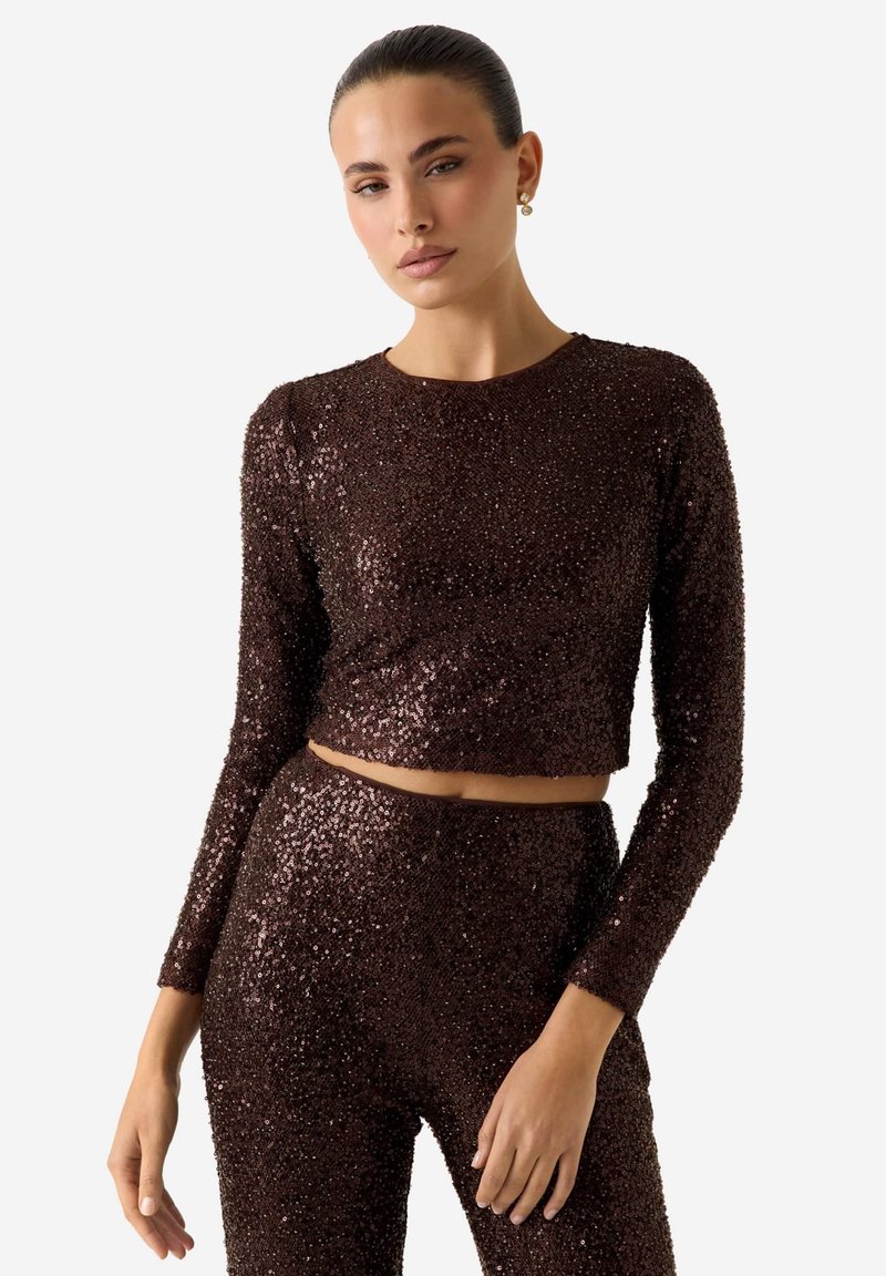 Top corto marrone in paillettes con maniche lunghe, caratterizzato da uno scollo rotondo e un design aderente. La superficie riflette la luce con una texture lucida.