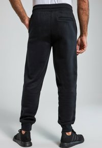 Pantalones de chándal negros hechos de una tela suave, con una cinturilla elástica, piernas ajustadas y un bolsillo en la parte posterior con detalle de costura.