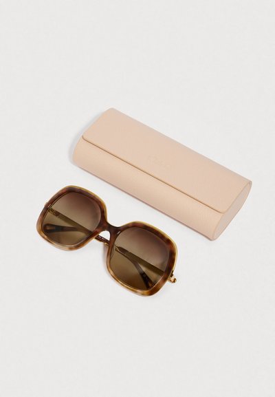 Sončna očala z okvirom iz žajbljeve lupine in rjavimi lečami z zatemnitvijo. Priložen je svetlo roza etui z teksturo in magnetskim zapiranjem.