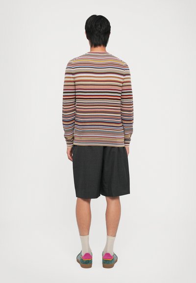 Pull rayé aux couleurs douces, short noir ample, et chaussures multicolores. Le pull a des manches longues et un col rond.