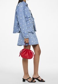 Farkkutakki, jossa on kukka-ompeluksia, mini farkkuhame, mustat korkeat sandaalit ja pieni punainen nahkainen käsilaukku kiristysnauhalla.