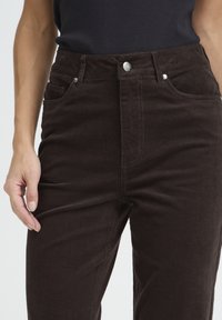 Brown corduroy pants with a high waist, five pockets, and silver hardware accents. The fabric features distinct vertical ribbing.