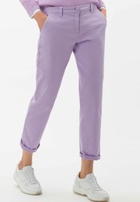 Lila bomullshängselbyxor med avslappnad passform, uppvikta fållar, sidofickor och knäppning. Bärs med vita sneakers för kontrast.