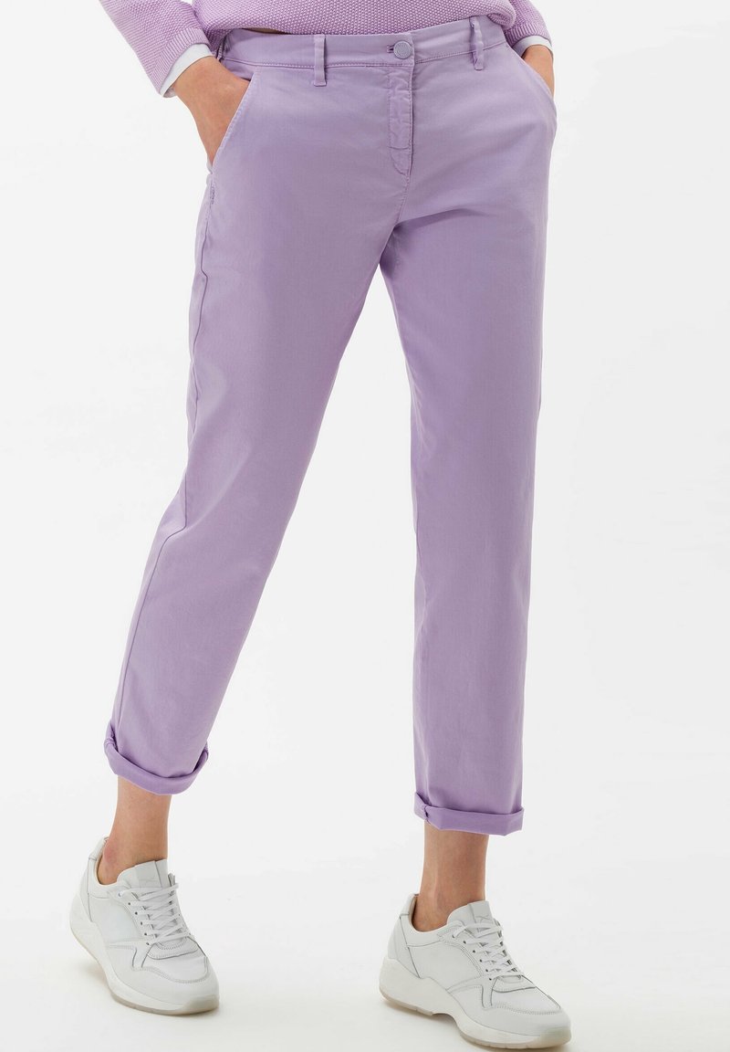 Lila bomullshängselbyxor med avslappnad passform, uppvikta fållar, sidofickor och knäppning. Bärs med vita sneakers för kontrast.