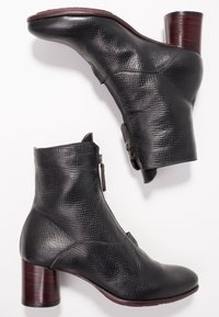 Černé texturované kožené kotníkové boty se zipy na stranách a s dřevěnými blokovými podpatky na bílém pozadí.