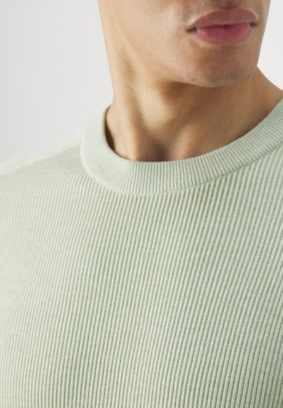 Lysegrønn ribbestrikket genser med rund hals. Nærbilde viser tekstur og subtile detaljer i stoffet. Myk og figurnær design.