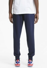 Marinblå joggerbyxor med mjuk textur, med nedhasade fållar och avslappnad passform, i kombination med sportiga sneakers i rött, vitt och blått.