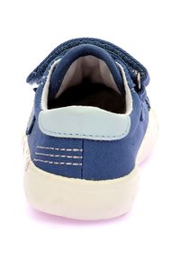 Zapatilla de lona azul con suela de goma blanca, que cuenta con un talón cosido, un detalle en azul claro en el talón y un cierre de correa simple.