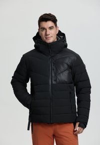 Chaqueta puffer negra con capucha, que cuenta con un bolsillo en el pecho con cremallera, diseño de acolchado horizontal y texturas mate y brillantes contrastantes.