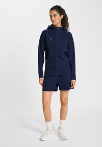 Mörkblå sportkläder med en zip-up huva jacka och matchande shorts i mjukt, töjbart tyg; med logotypdetalj.