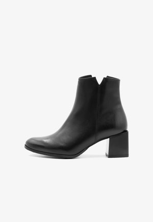 Bottine en cuir noir à bout pointu, avec un talon bloc et un décolleté en V à la cheville, présentant une texture lisse et un design minimal.