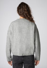 Gray, soft-knit sweater with a round neckline and dropped shoulders, featured with a cropped fit and ribbed hem, worn over black jeans.