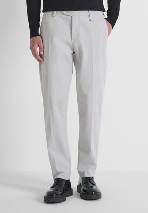 Lichtgrijze, gestreepte, op maat gemaakte broek met een losse pasvorm en zijzakken, gecombineerd met zwarte, schoenen met dikke zolen.