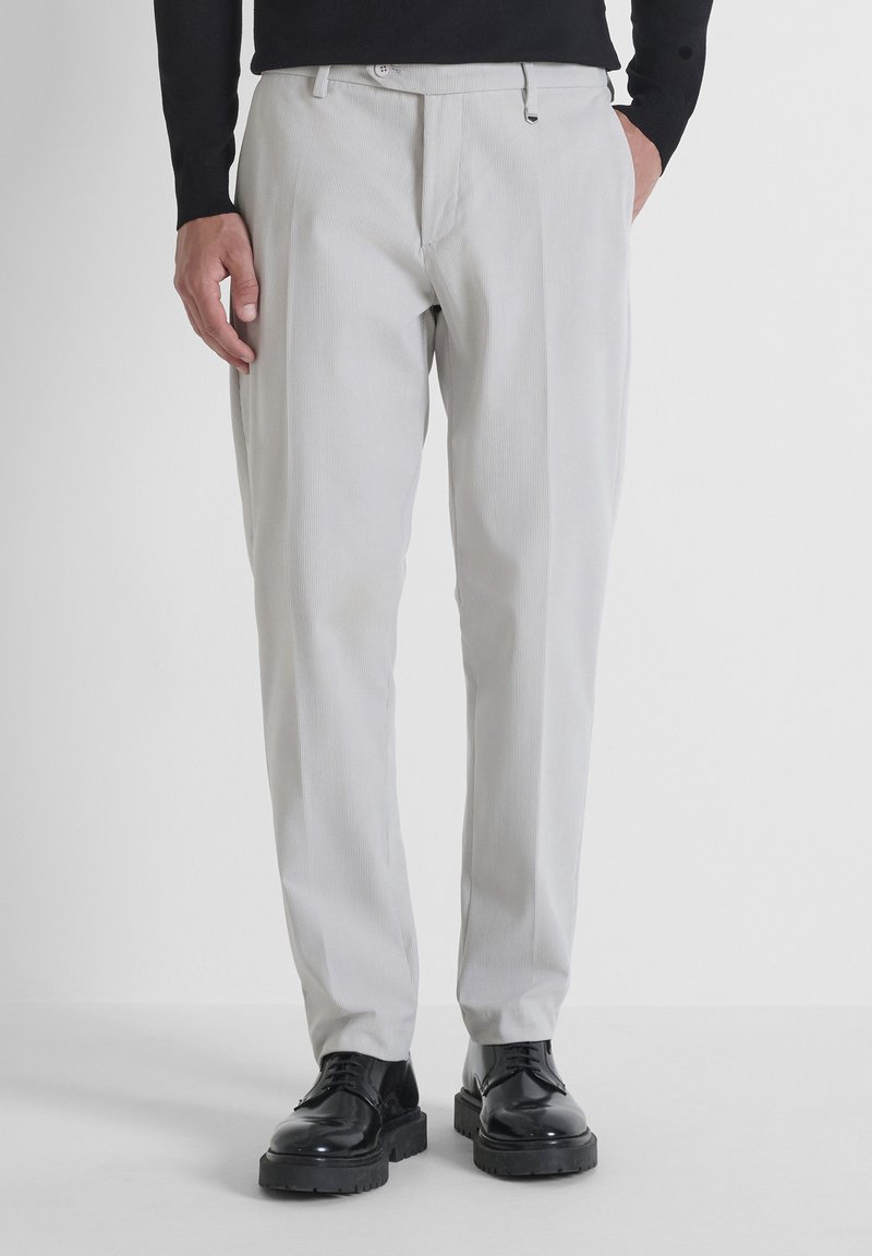 Lichtgrijze, gestreepte, op maat gemaakte broek met een losse pasvorm en zijzakken, gecombineerd met zwarte, schoenen met dikke zolen.