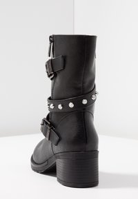 Botas negras de tobillo con un acabado de cuero texturizado. Las características incluyen doble hebilla, una correa con tachuelas y un tacón grueso. Cierre con cremallera lateral.