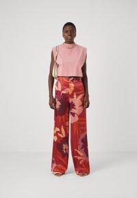 Rozā cropped tops ar platām plecu lencēm un ziedu raksta platām biksēm sarkanos, oranžos un rozā toņos. Vienkāršs kaklarota un plecu soma.