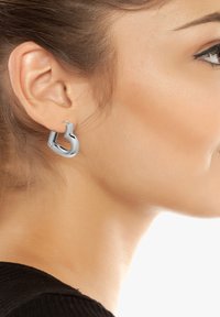 Boucles d'oreilles en argent en métal, dotées d'une forme de crochet unique. Texture lisse avec une finition brillante, conçues pour se clipser sur le lobe de l'oreille.