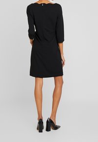 Černé šaty s tříčtvrtečními rukávy, detaily na zipu na zadní straně, pohodlným pasem a dlouhými po kolena. Nosené s černými botami na blokovém podpatku.