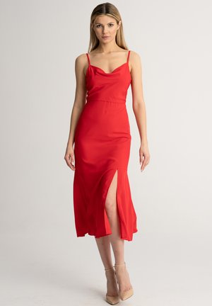 Abito rosso realizzato in tessuto liscio, con spalline sottili, scollo a barchetta e uno spacco alto fino alla coscia su un lato.