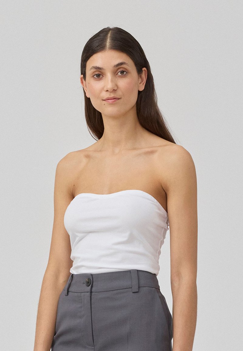 Haut sans bretelles blanc en tissu lisse, associé à un pantalon taille haute gris. Le haut a une coupe ajustée avec un décolleté droit.