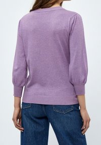 Lila stickad pullover med ballongsleeves, ribbade muddar och nederkant. Tyget verkar mjukt och lätt, utformat för avslappnad användning.