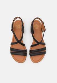Sandales en cuir noir avec plusieurs sangles, un design texturé, et un pied rembourré tan. Fermeture à boucle sur la sangle de la cheville.