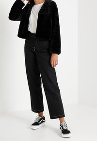 Svart faux fur kort jacka över en vit t-shirt, kombinerad med högmidjade svarta vida byxor och svart-vita sneakers.